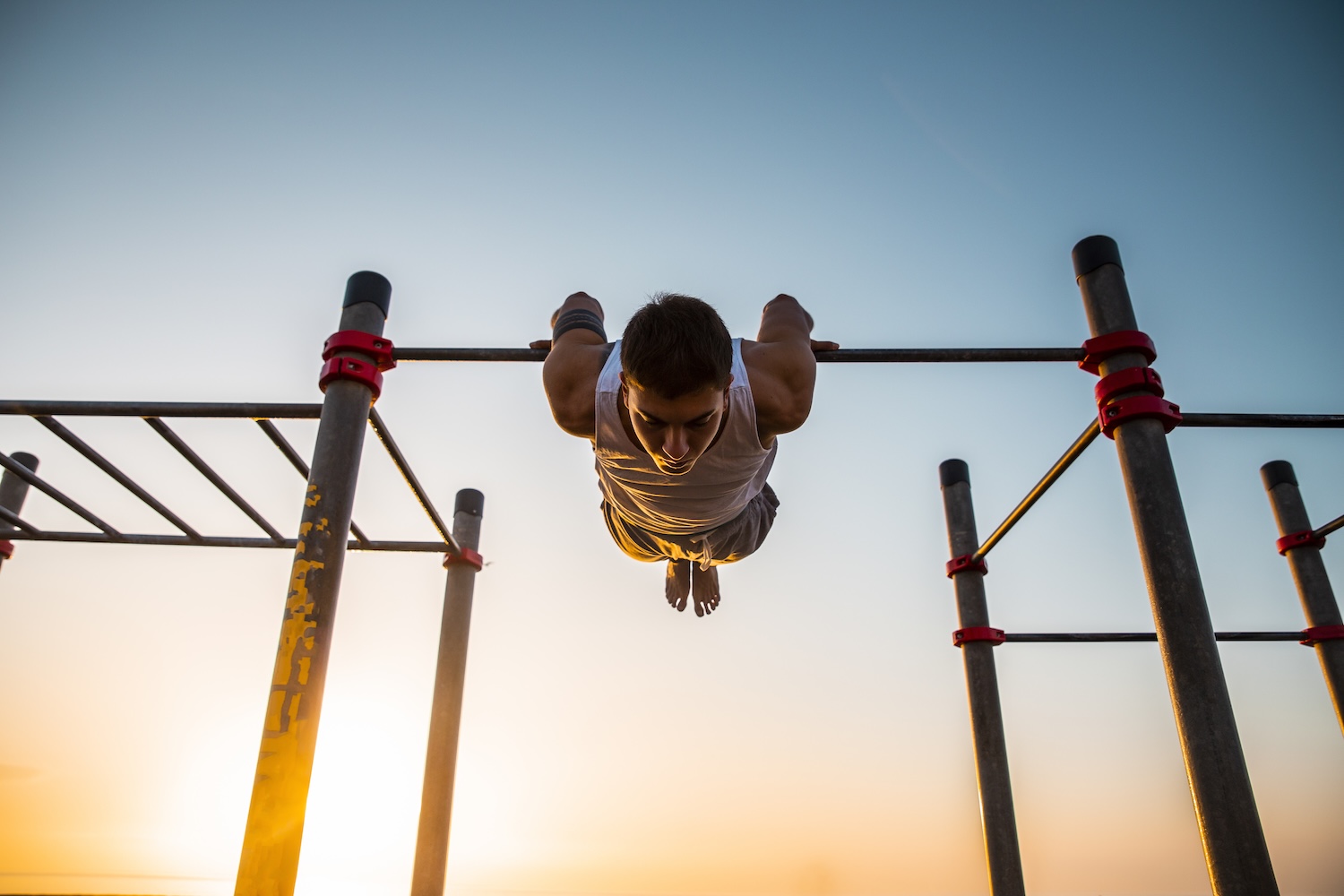 Young man practicing calisthenics at an outdoor gym at sunrise Young man practicing calisthenics at an outdoor gym at sunrise